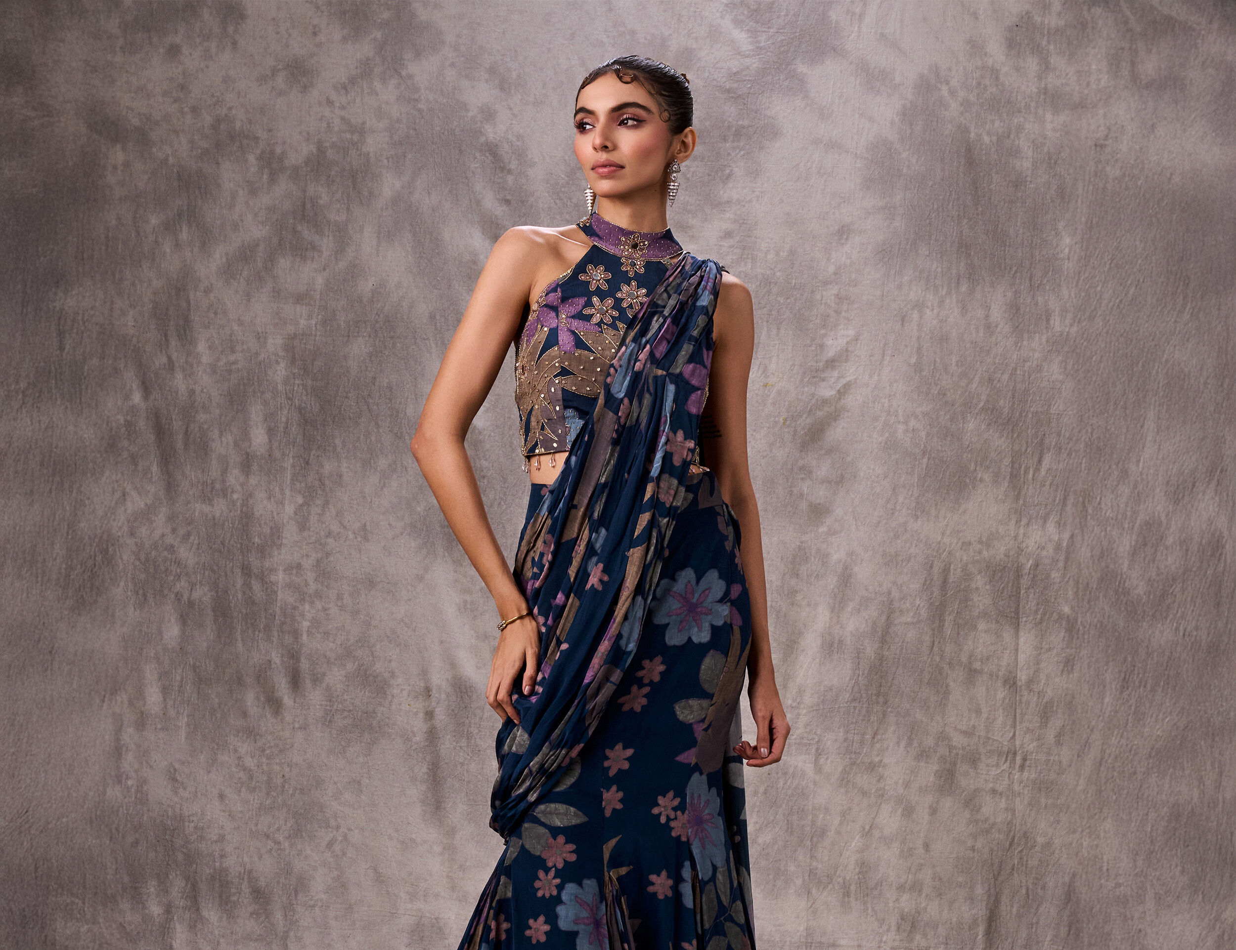 Woman modeling a floral printed blue saree with a high-neck embroidered blouse, showcasing a chic blue-on-blue combination.